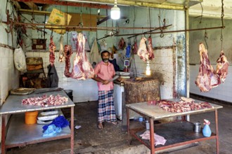 Butcher in traditional slaughterhouse with pieces of meat hanging on hooks, The old market halls of