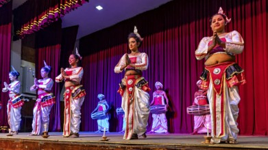 Artists in colorful traditional clothing dance on a stage in front of a red curtain, folklore and