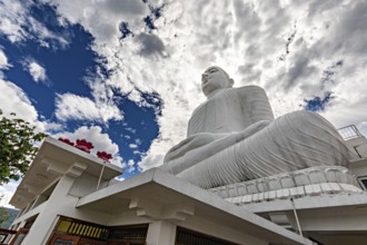 Large white Buddha statue under dramatic sky surrounded by temple architecture and clouds, white