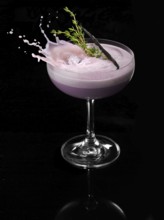 An ice cube cube falls into a cocktail cup and allows the liquid to splash on, studio shot against