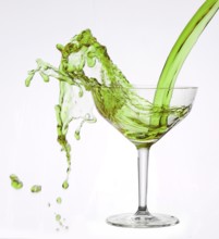 A powerful flood of green liquid pours into a cocktail glass and spills over, studio shot against a