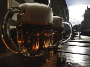 Beer mugs on a table at sunset with an urban backdrop in the background, Pilsen, Czech Republic
