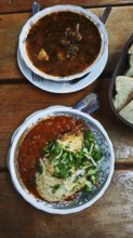 Two bowls of soup, Kharcho, served on a wooden table, one with chunky stew and the other with a red
