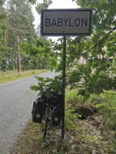 Bicycle with luggage bags in front of a Babylon town sign on a road through the forest, Czech