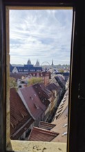 Through a window, a view of an urban landscape with roofs, church towers and a Ferris wheel,