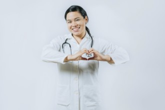 Smiling asian female doctor making heart shape isolated. Asian healthcare worker gesturing heart