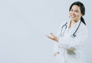 Smiling asian female doctor showing empty space isolated. Young asian doctor presenting something