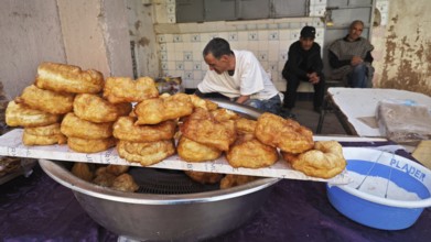 Fried pastries on a market stand surrounded by people in a street area, southern Morocco