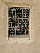 Decorated window screen in a crumbling, beige clay wall with rustic ambiance, Morocco