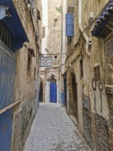 Narrow old town alleyway with weathered doors and the sign of a dentist, dentist, under a blue sky,