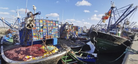 Fishing boats with colorful boxes and nets in quiet harbor under blue sky, Essaouira, Morocco
