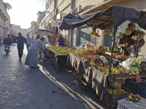 Bustling market street with stalls full of fresh fruit and people shopping, Morocco