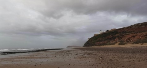 Empty beach with cloudy sky and rocky coast in the background, Morocco
