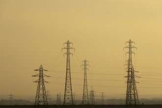 Electricity pylons and power lines silhouette at sunset, England, United Kingdom