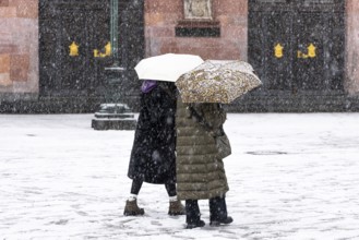 Two passers-by walk across Frankfurt's Römerberg with umbrellas. Heavy snowfalls have caused