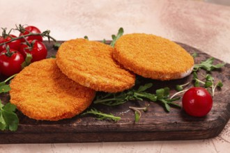 Crispy fried fish cutlets, fish burgers, on a wooden chopping board, with arugula and cherry