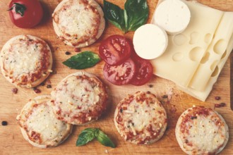 Freshly baked mini pizza, on a wooden board, with fresh vegetables and cheese, top view
