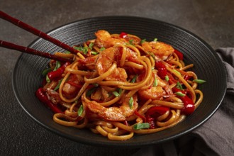Udon stir-fry shrimp noodles with red bell pepper and green onion, served in a black bowl, with