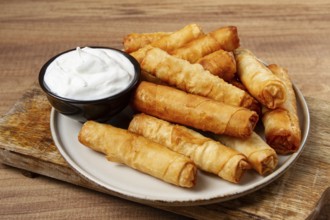 Fried spring rolls with cheese, on a wooden background, with cream sauce, no people