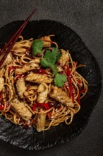 Udon noodles, with squid and vegetables, on a black plate, homemade, no people
