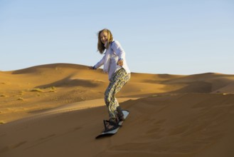 Young woman with snowboard in the sand dunes, near Merzouga, Meknès-Tafilalet region, Erg Chebbi,