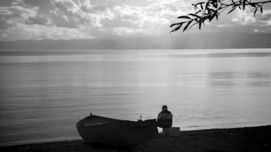 Lonely person on lake shore with boat and calm water surface in black and white, Ohrid Lake, North