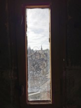View through a narrow window of a city with church towers and a Ferris wheel under a cloudy sky