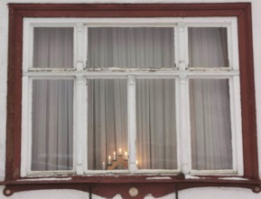 Rustic window with red wooden frame and candles inside, creates a cozy evening mood