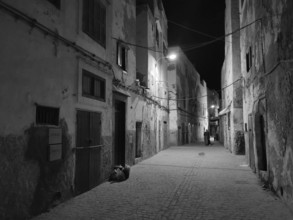 Nighttime scene of a quiet alley illuminated by a few alleyway lamps in black and white, Essaouira,