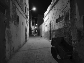 Abandoned old alley in nighttime darkness, faintly lit by black and white lanterns, Essaouira,