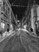 Night view of a paved street with tram tracks and illuminated buildings in black and white, Lisbon,
