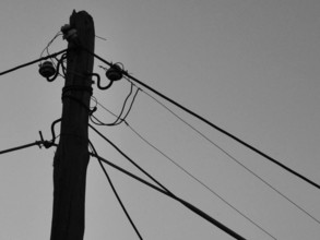Close-up of an old wooden power pole with several wires against the sky, black and white, Berat,