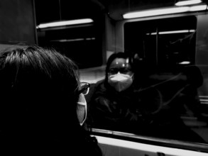 A person wearing a mask looks at their reflection in a train window during corona, black and white,