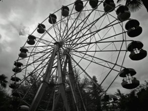 Silhouette of a Ferris wheel against a cloudy sky in a black and white theme park, Kutaisi, Georgia