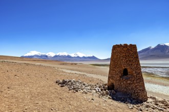 Ancient stone structure in a vast desert landscape with snowy mountains in the background, The