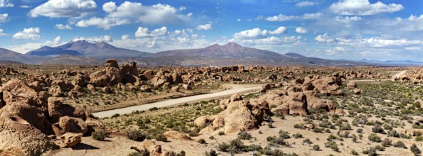 Wide panoramic landscape with large rocks, a dusty desert and mountains under a cloudy sky, The