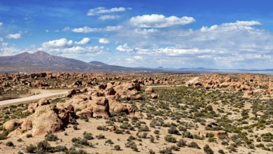 Desert landscape with a road leading through rocks and mountains, under a sky with clouds, The
