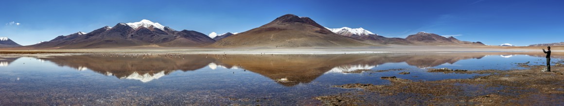 Wide panorama of mountains with reflecting lake and clear sky above the scene, Laguna Colorada in