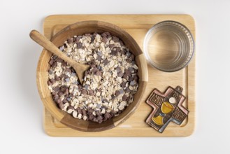 Wooden bowl with cereal and a cross on a wooden board with water, fasting