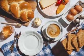 Breakfast with toast, stollen, honey, cheese, ham, coffee, butter, peppers and eggs on a table