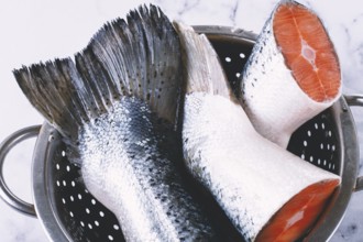 Fish tails are placed in a colander on a marble counter. The colander allows water to drain away