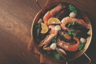 Seafood and black rice paella, in a frying pan, homemade, on a wooden table, no people