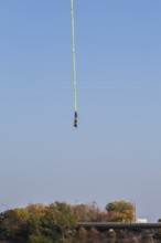 Female bungee jumper in midair with her ankles tied to a long yellow elastic bungee jumping cord,
