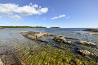 Clear sky over rocky archipelago coastline with granite archipelago with green forest and blue