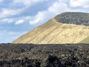 Hiking trail through lava rock to Caldera Blanca volcano against blue sky with white clouds, Mancha