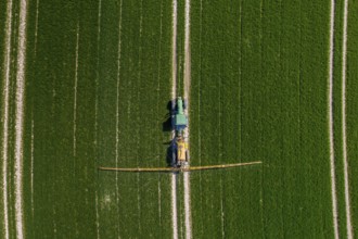 Aerial view over agricultural trailed field sprayer pulled by tractor spraying crop on farmland,