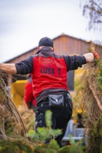 Back view of a man in work clothes carrying branches with a building in the background, tree work,