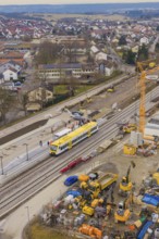 Construction site with crane and yellow train at a municipal train station, surrounded by