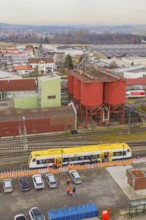 Aerial view of an industrial area with a yellow train and large red buildings, taking the Hermann