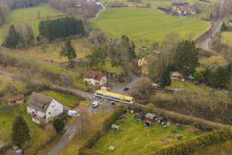 Rural scene with yellow train on rails, surrounded by trees and houses in the countryside,
